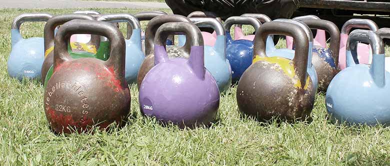 Különböző súlyú kettlebell golyók egymás mellett a fűven.